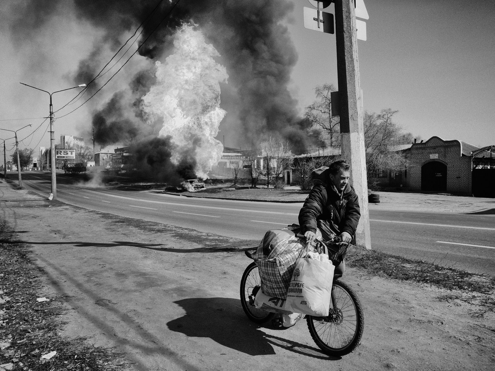 A person pushing a bike with a large fire behind them.