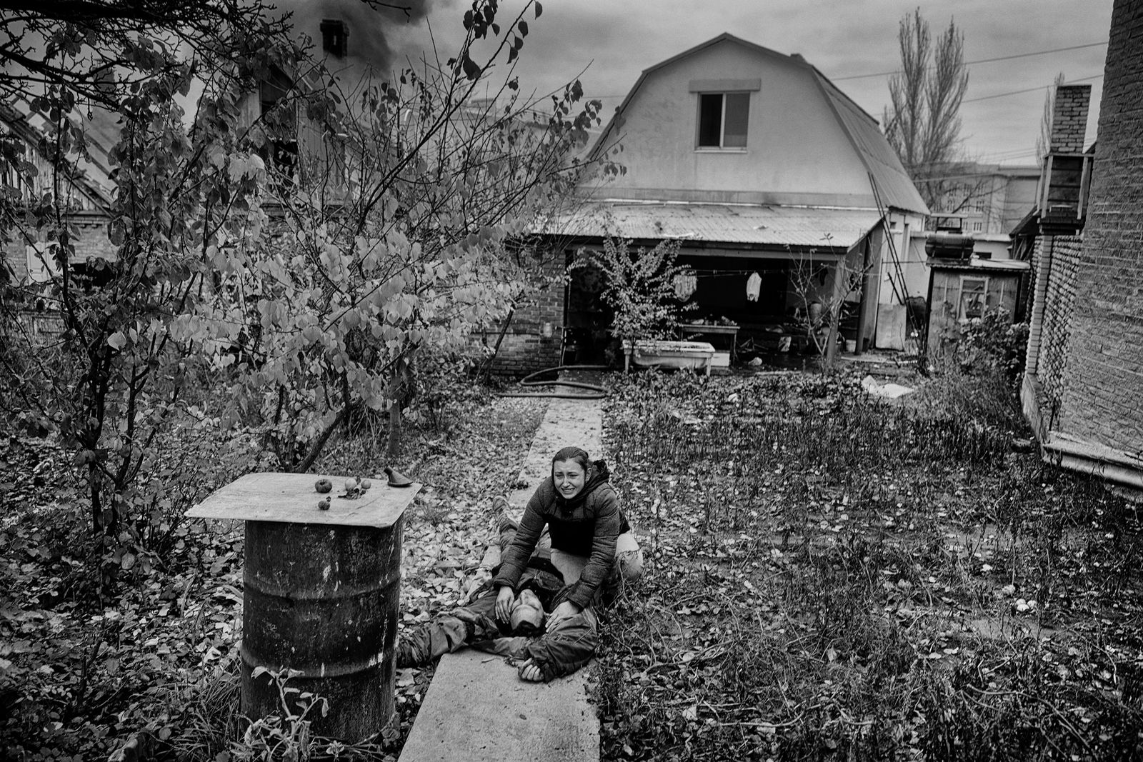 A woman leaning over a dead body on a path to a house.