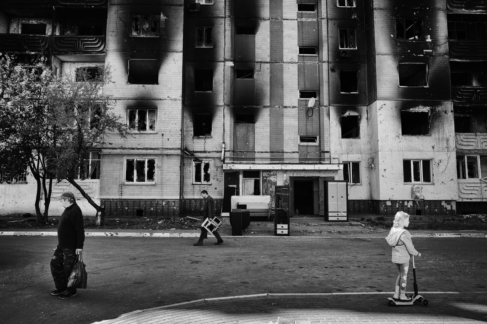People walking in front of a burned building.
