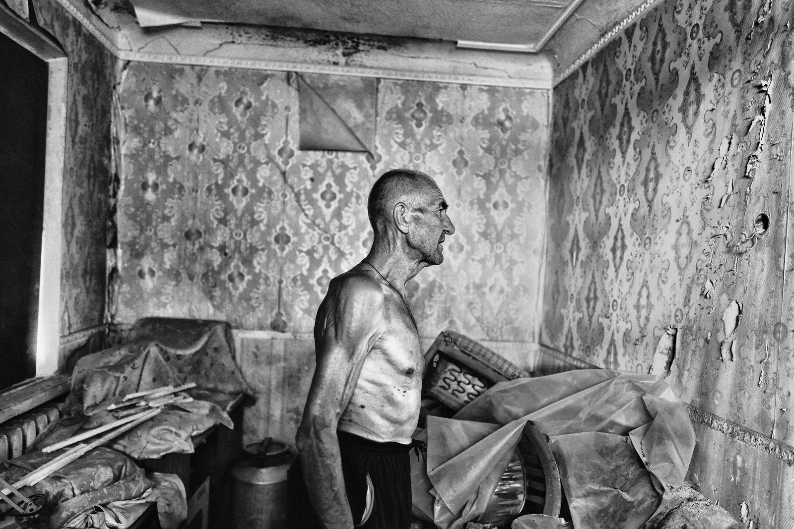 A shirtless man in a room full of debris.