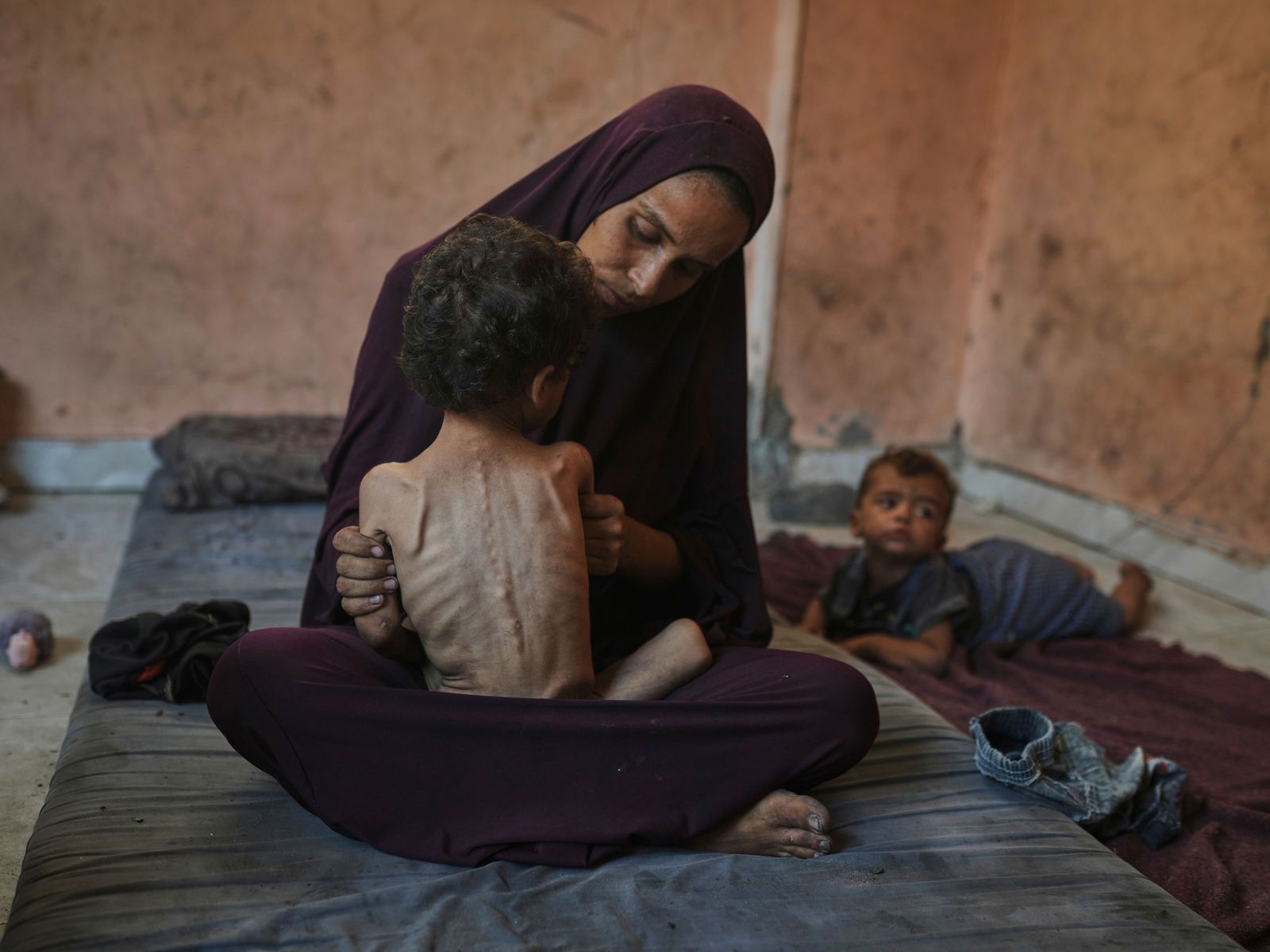 Photograph of a mother holding her child in her lap with a baby laying the background.