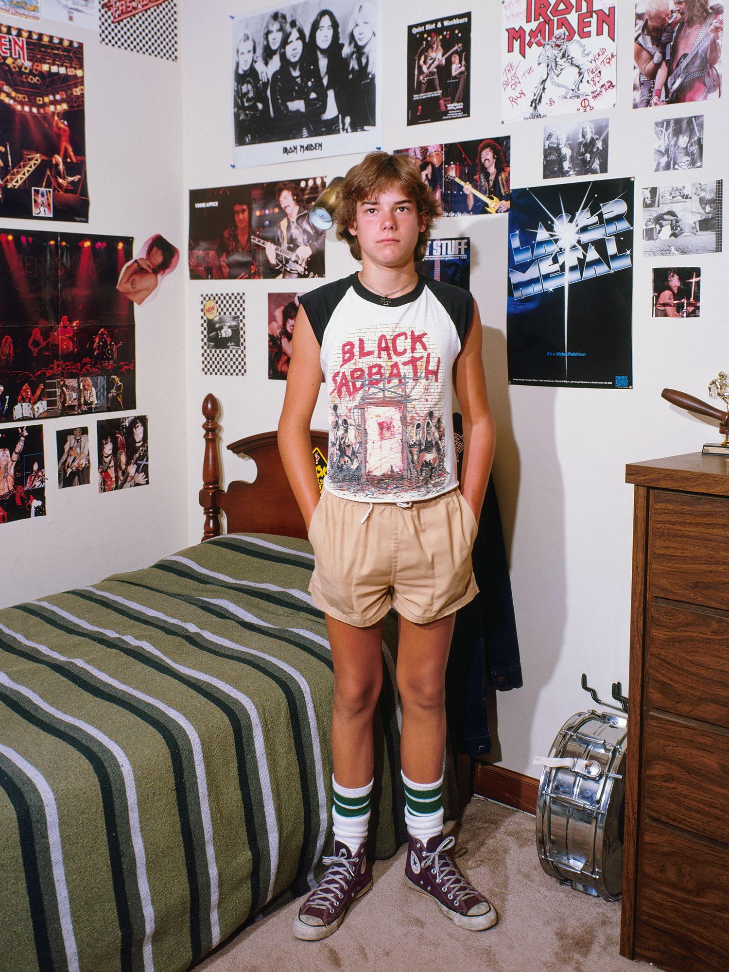 A young man wearing a Black Sabbath tshirt in a room full of posters.