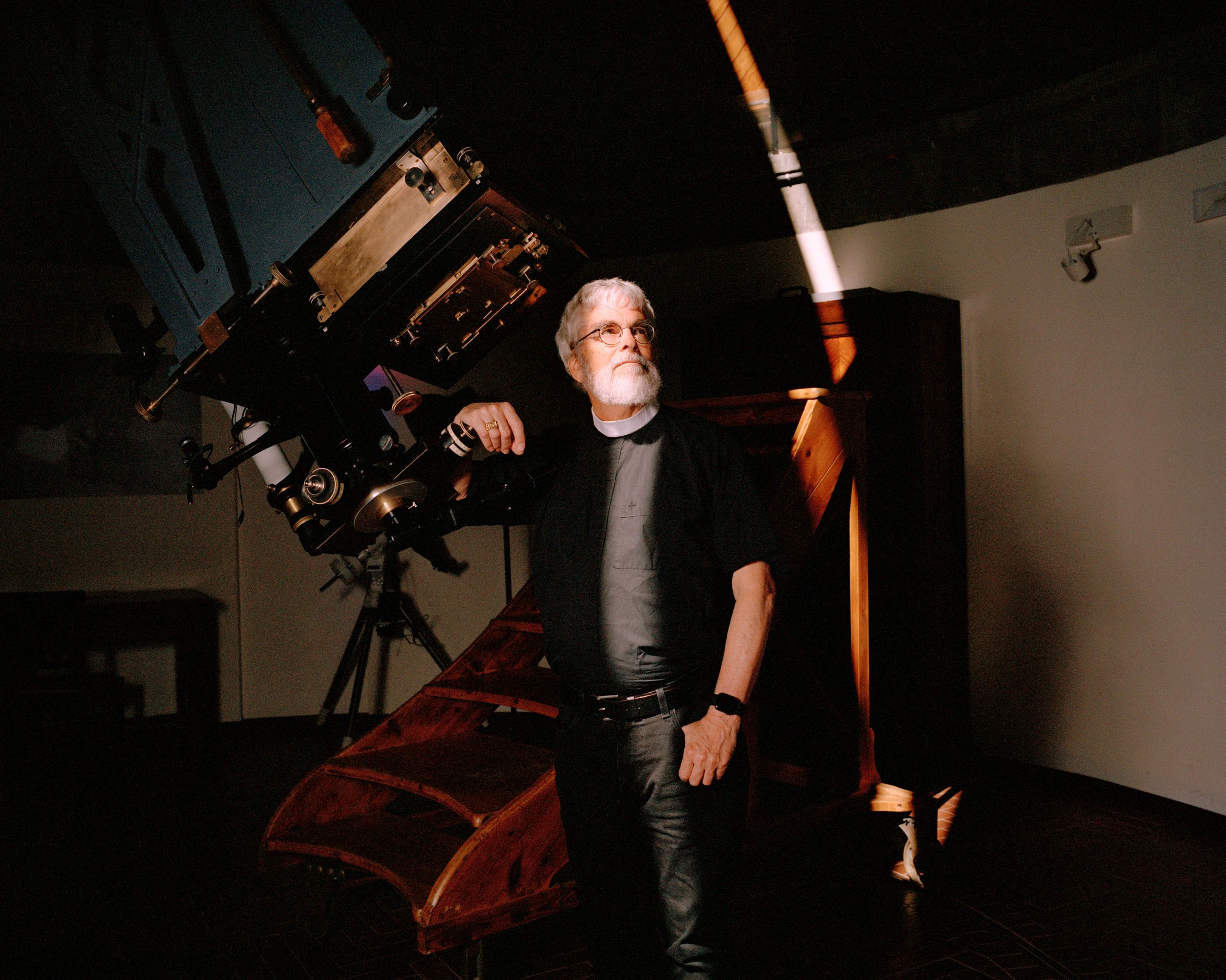 A photo of a man in religious attire leaning against a telescope.